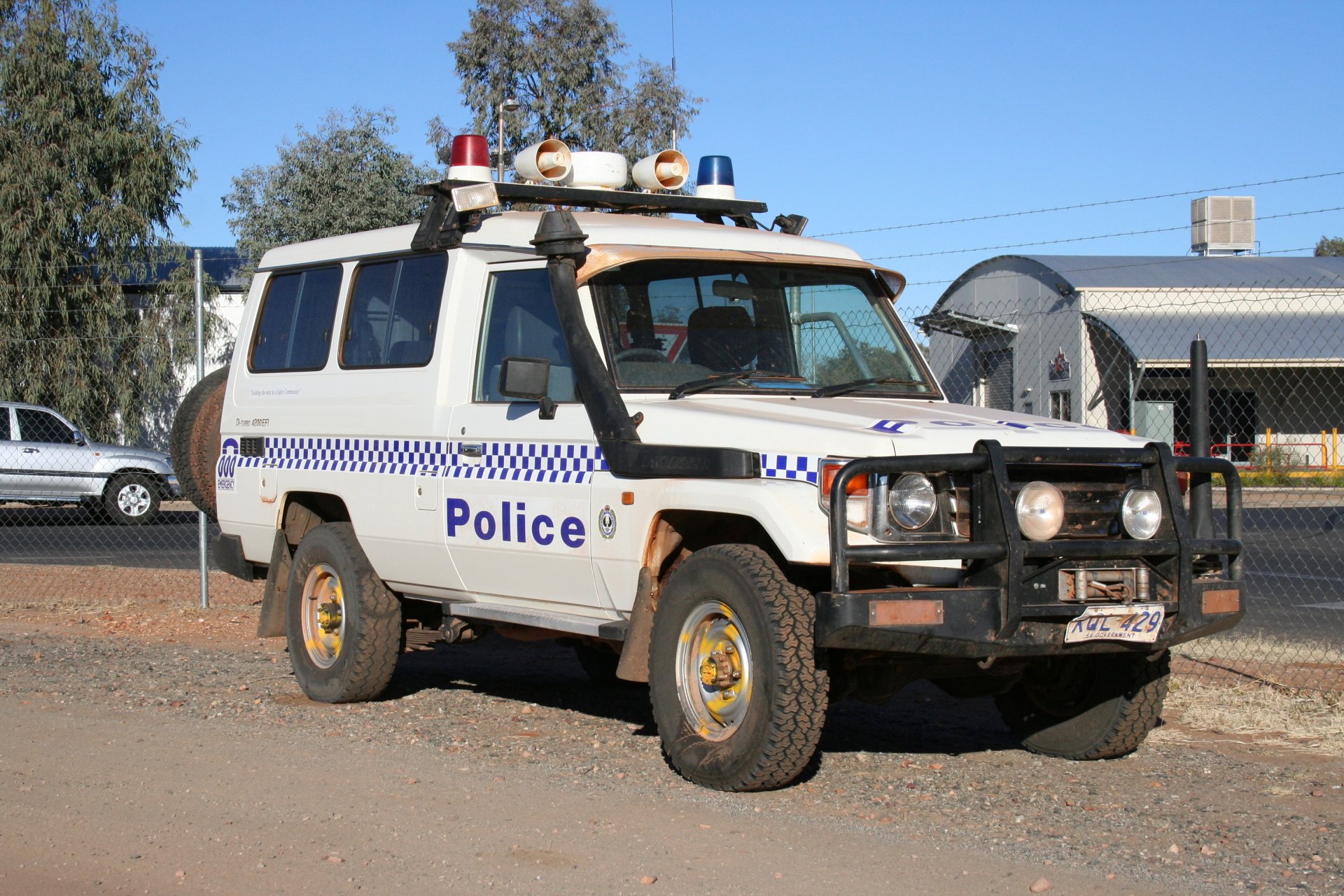 HD desktop wallpaper featuring a white police vehicle parked outdoors on a sunny day with clear blue skies and surrounding buildings.
