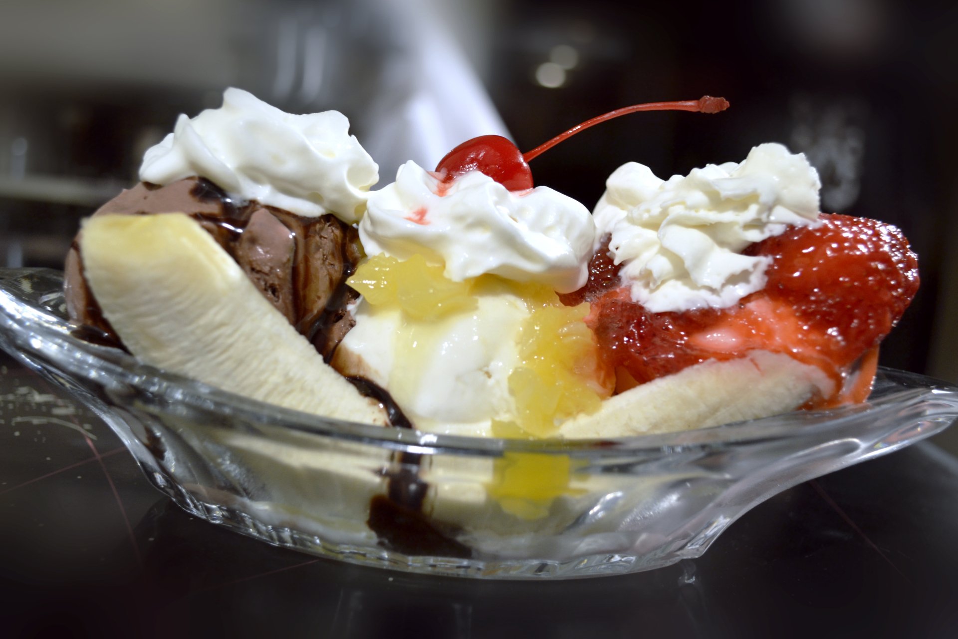 4K Ultra HD PC desktop wallpaper of a banana split: three scoops of ice cream with chocolate, pineapple and strawberry sauces, whipped cream and cherries in a glass dish.