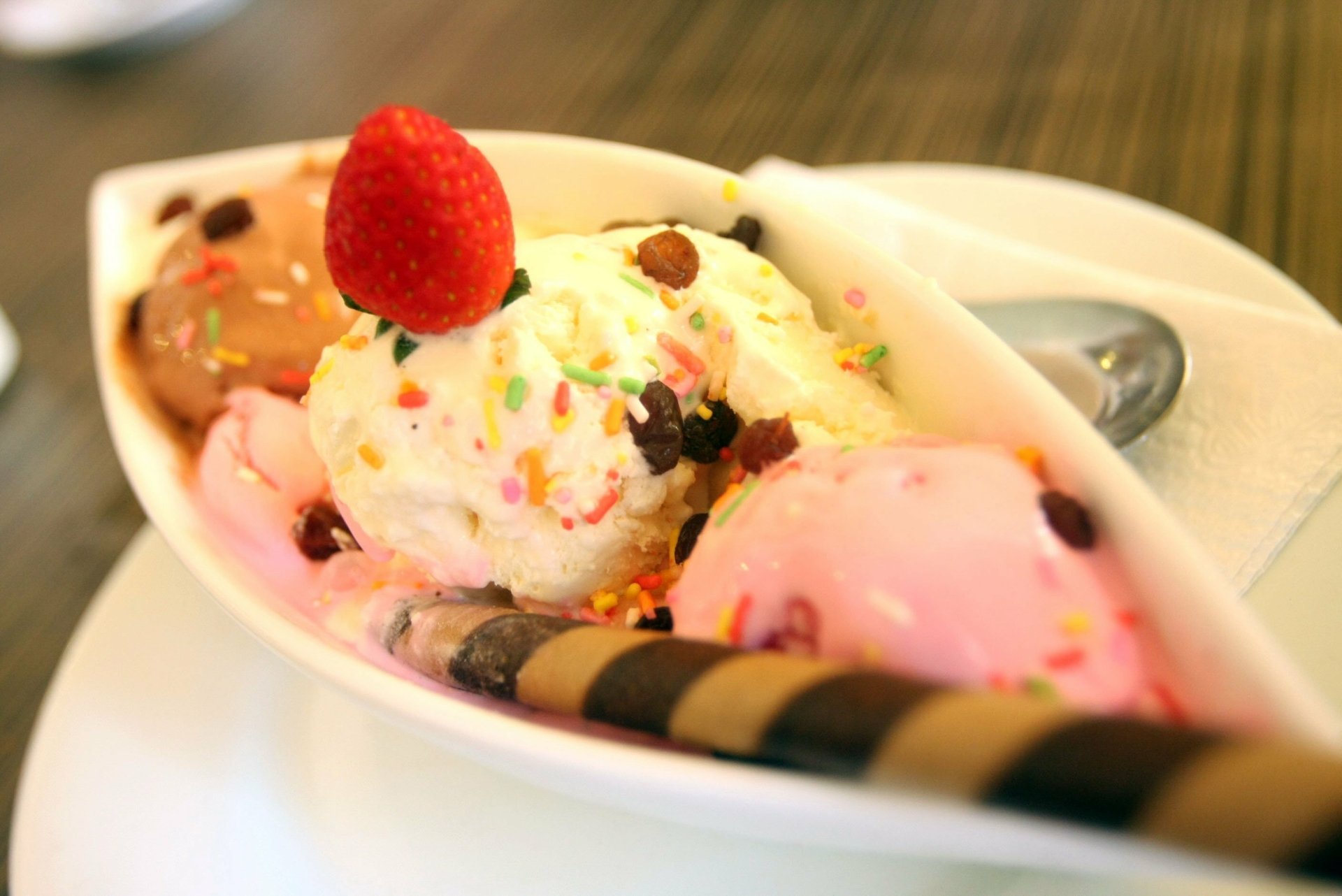 A vibrant HD desktop wallpaper featuring a colorful banana split with scoops of ice cream, whipped cream, sprinkles, a strawberry, and a chocolate wafer on a white plate.