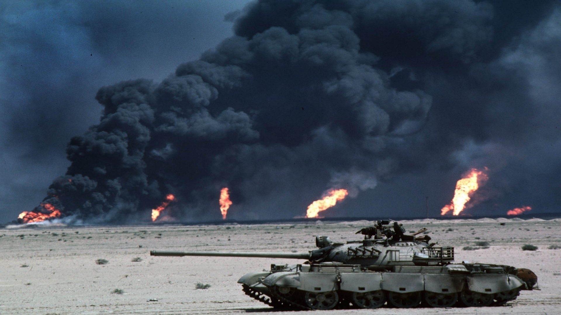 HD PC desktop wallpaper: military tank in desert with billowing smoke and burning oil fires, Gulf War battlefield background.