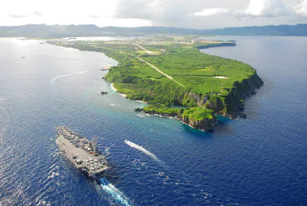 A 4K Ultra HD image of the USS Ronald Reagan (CVN-76), a military aircraft carrier, sailing near a lush green island coastline.