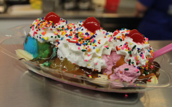 Banana split topped with whipped cream, colorful sprinkles, three cherries, and scoops of ice cream, shown in vibrant 4K Ultra HD as a PC desktop wallpaper.