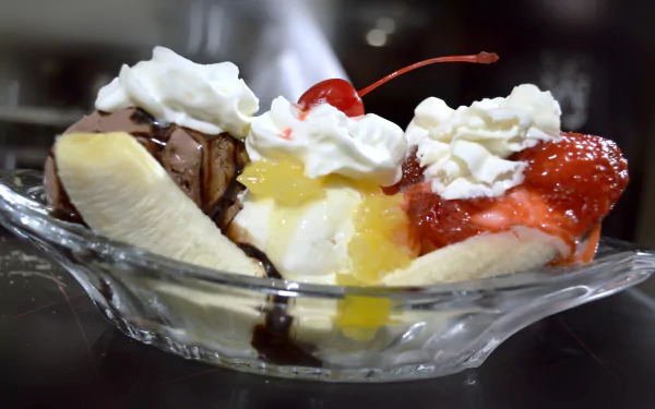 4K Ultra HD PC desktop wallpaper of a banana split: three scoops of ice cream with chocolate, pineapple and strawberry sauces, whipped cream and cherries in a glass dish.