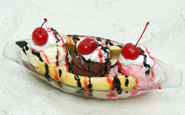 4K Ultra HD PC desktop wallpaper of a banana split: vanilla, chocolate and strawberry scoops with cherries and drizzled chocolate and strawberry syrup in a glass dish.