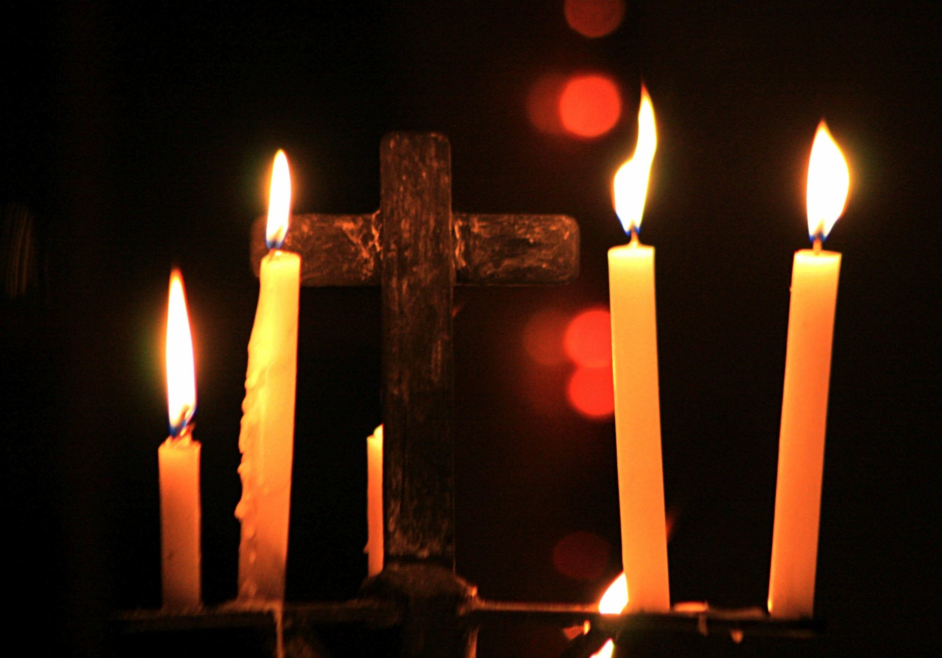 2K Quad HD PC desktop wallpaper photography: silhouetted cross with glowing candles and warm flames, soft red bokeh against a dark background.