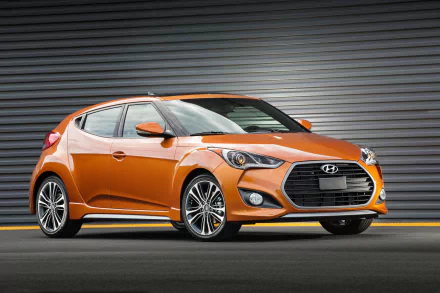 Orange Hyundai Veloster car parked in front of a metal shutter, shown in a high-definition PC desktop wallpaper background.
