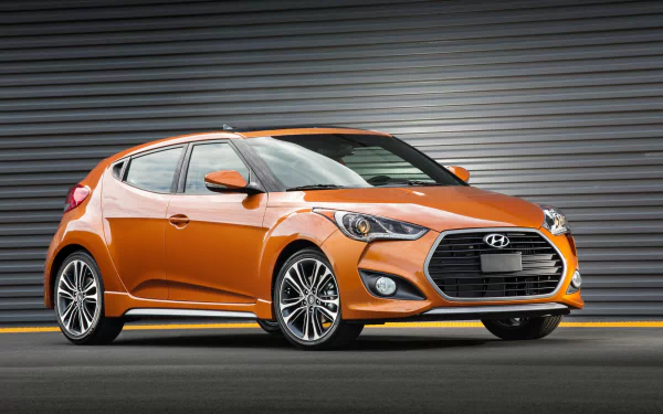 Orange Hyundai Veloster car parked in front of a metal shutter, shown in a high-definition PC desktop wallpaper background.