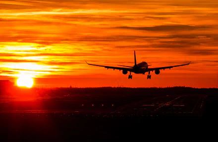 An Airbus A330 approaches an airport against a vibrant orange sunset, showcasing the silhouette of the airplane in the sky. This HD image captures a tranquil travel moment.