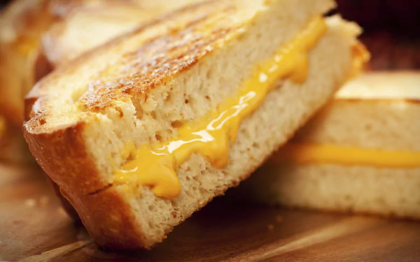 Close-up of a gooey grilled cheese sandwich with melted cheddar between golden toasted bread, captured in 4K Ultra HD for a vibrant PC desktop wallpaper.
