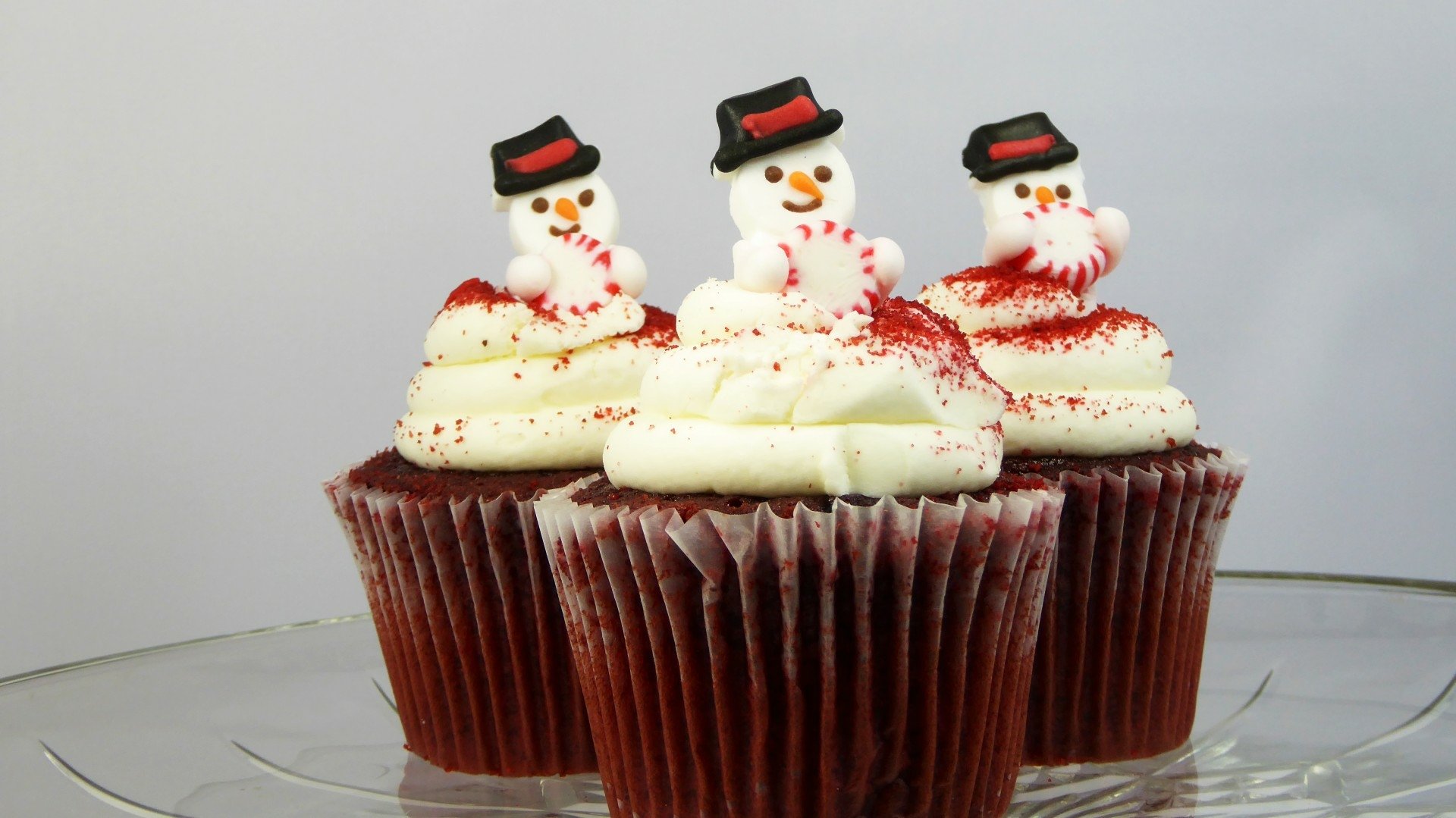 Three Christmas-themed cupcakes topped with snowman decorations and white frosting, presented as a HD PC desktop wallpaper background.