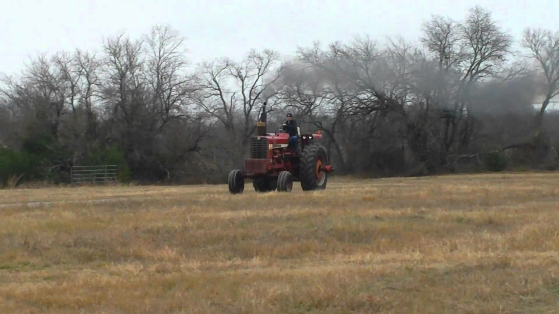 HD PC desktop wallpaper featuring a red tractor driving across a field with bare trees and an overcast sky in the background.