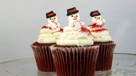 Three Christmas-themed cupcakes topped with snowman decorations and white frosting, presented as a HD PC desktop wallpaper background.