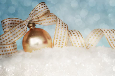 A festive holiday scene featuring a golden Christmas ornament nestled in snow, adorned with a delicate ribbon, creating a vibrant 4K Ultra HD desktop wallpaper for the season.