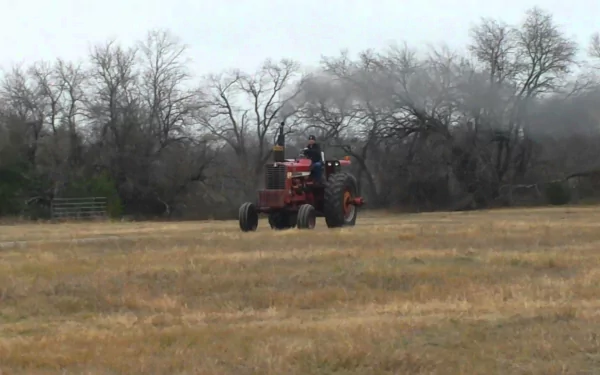 HD PC desktop wallpaper featuring a red tractor driving across a field with bare trees and an overcast sky in the background.