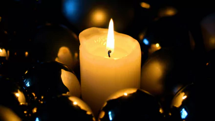 A glowing candle surrounded by shiny Christmas balls, casting warm light and reflections, captured in a 4K Ultra HD holiday-themed desktop wallpaper.