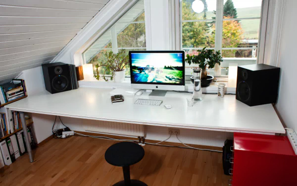 4K Ultra HD PC desktop wallpaper: bright attic room with man-made white desk, monitor displaying a scenic image, studio speakers, plants, books and a stool.