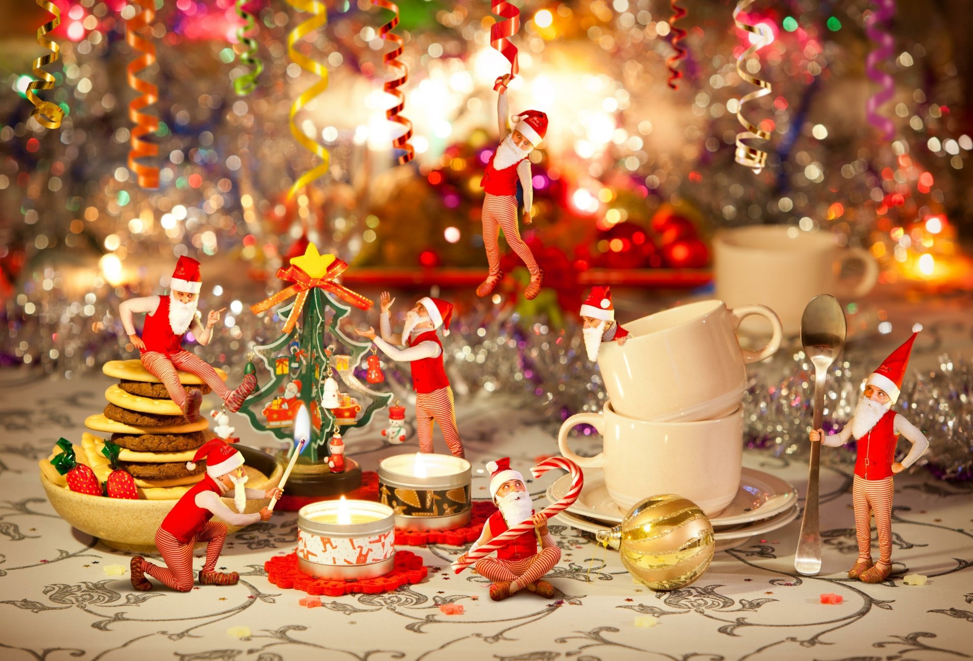 A festive 4K Ultra HD PC desktop wallpaper featuring playful elves with Christmas decorations, cookies, candles, and holiday cups amid sparkling background lights.