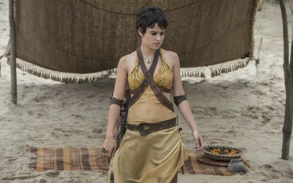 Tyene Sand, portrayed by Rosabell Laurenti Sellers, stands on a sandy beach in a striking outfit, set against a backdrop of a tent in this 4K ultra HD Game of Thrones wallpaper.