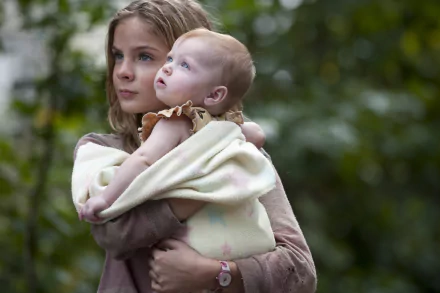 HD desktop wallpaper of Lizzie Samuels, played by Brighton Sharbino, holding a baby in a scene from the TV show The Walking Dead, set against a natural outdoor background.