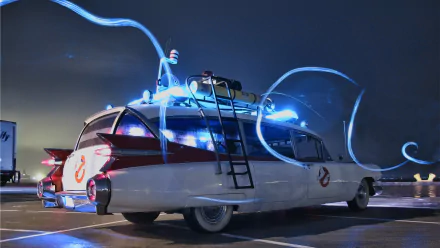 HD PC desktop wallpaper: Ghostbusters Cadillac Superior Ecto parked at night, roof gear lit and trailing blue proton light effects against a dark sky.