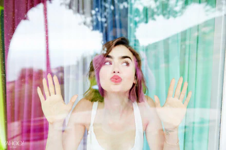 English actress Lily Collins with short brunette hair presses her face and hands against a glass window, captured in vibrant 4K Ultra HD quality for a desktop wallpaper.