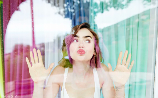 English actress Lily Collins with short brunette hair presses her face and hands against a glass window, captured in vibrant 4K Ultra HD quality for a desktop wallpaper.