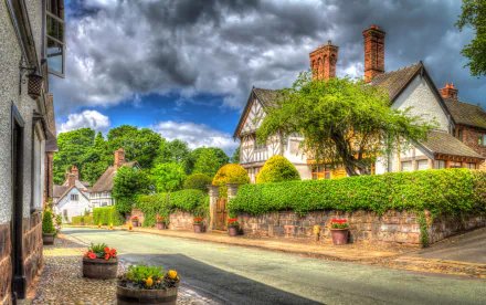 A picturesque street in England featuring charming houses, lush trees, and vibrant flower pots under a dramatic sky, captured in stunning HDR quality for a captivating desktop background.
