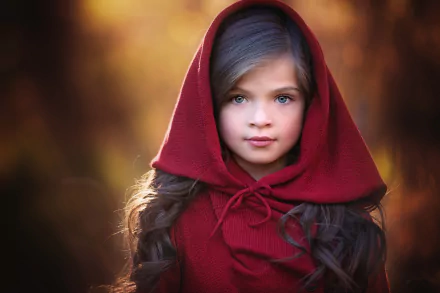 HD desktop wallpaper featuring a child with blue eyes wearing a red hooded cloak, set against a softly blurred, warm-toned background in a photography style.