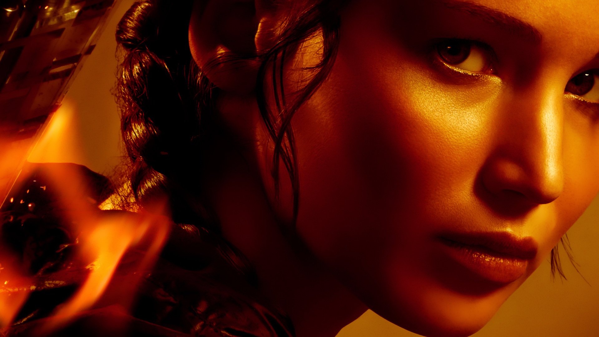Close-up of Katniss Everdeen from The Hunger Games movie, featured in an HD PC desktop wallpaper with warm tones and intense expression.