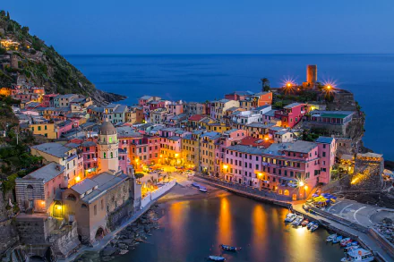 Dusk view of Vernazza, a colorful man-made village in Cinque Terre, Italy, with illuminated buildings along the coastline and calm waters, captured in HD for a desktop wallpaper.
