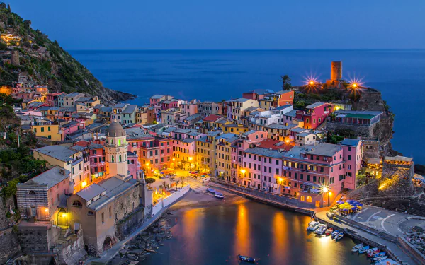 Dusk view of Vernazza, a colorful man-made village in Cinque Terre, Italy, with illuminated buildings along the coastline and calm waters, captured in HD for a desktop wallpaper.