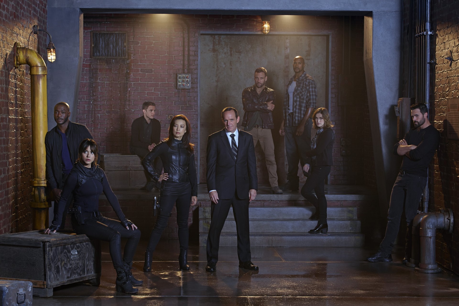 A dramatic scene from Marvel's Agents of S.H.I.E.L.D., featuring a group of characters posing confidently in a dimly lit urban setting with industrial elements.