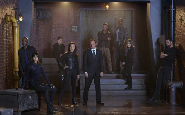 A dramatic scene from Marvel's Agents of S.H.I.E.L.D., featuring a group of characters posing confidently in a dimly lit urban setting with industrial elements.
