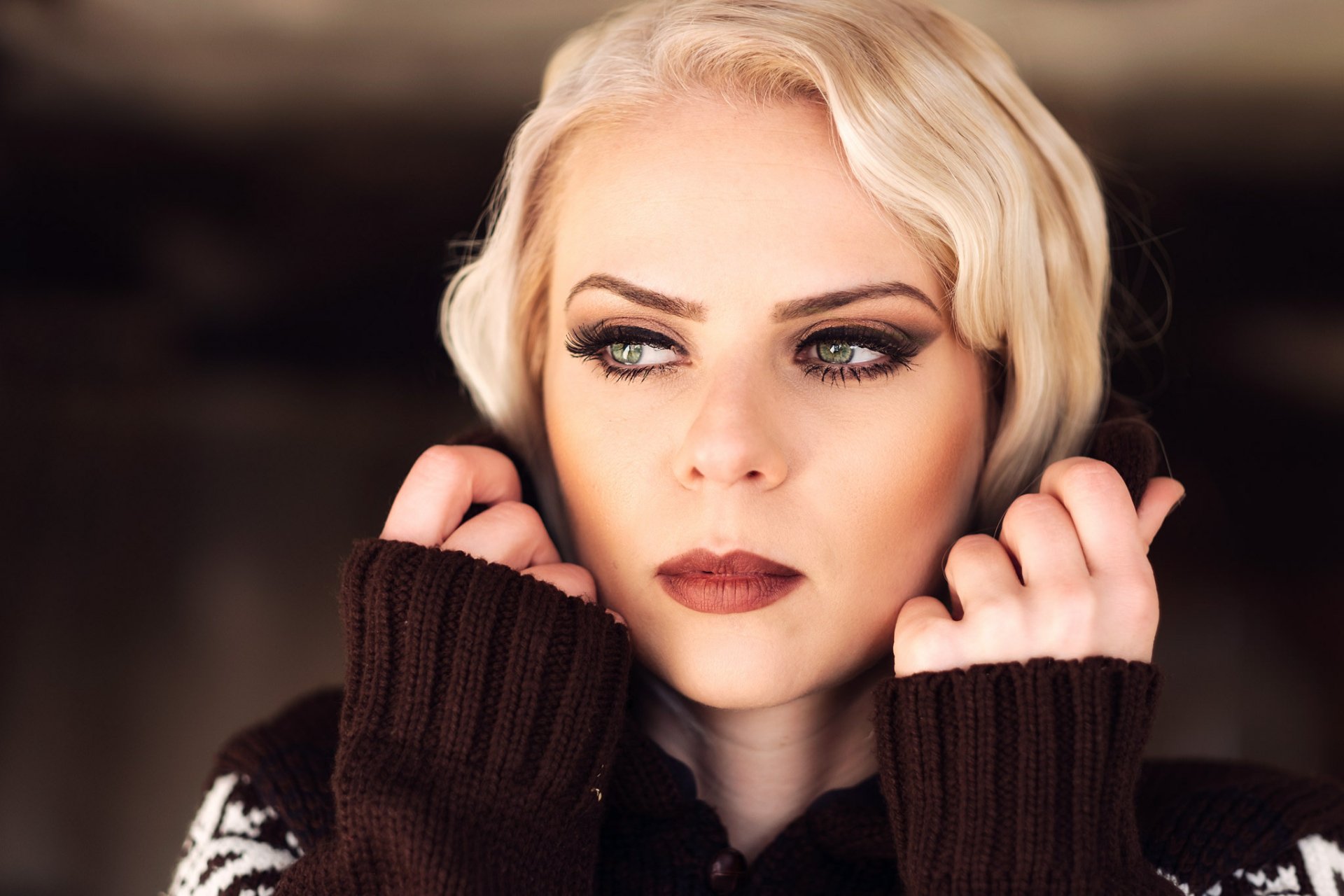 HD PC desktop wallpaper: close-up of a blonde woman/model with green eyes and dark lipstick, hands framing her face against a soft bokeh background.