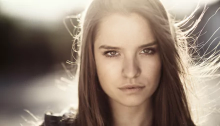 Close-up HD portrait of a brunette woman with brown eyes, softly lit by sunny bokeh, captured as a striking PC desktop wallpaper background.