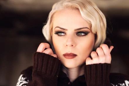 HD PC desktop wallpaper: close-up of a blonde woman/model with green eyes and dark lipstick, hands framing her face against a soft bokeh background.