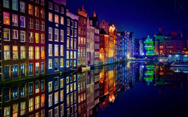 A vibrant night scene of Amsterdam's iconic colorful buildings along the canal, beautifully reflected in the water, creating a stunning HD desktop wallpaper.
