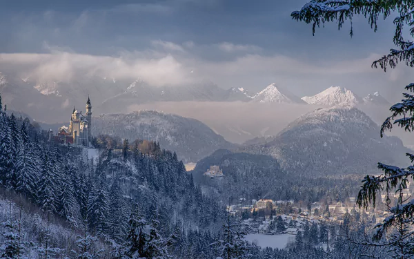 A breathtaking winter landscape of Neuschwanstein Castle in Germany, surrounded by snowy mountains and dense evergreen trees, creating a serene and picturesque scene.