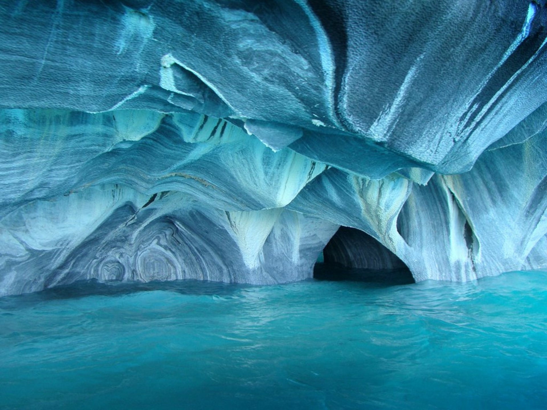 HD PC desktop wallpaper showing a stunning natural cave with smooth, swirling blue rock formations over clear turquoise water.