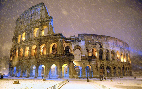 HD desktop wallpaper of the man-made ruin, the Colosseum, illuminated in snowy weather against a dusky sky.