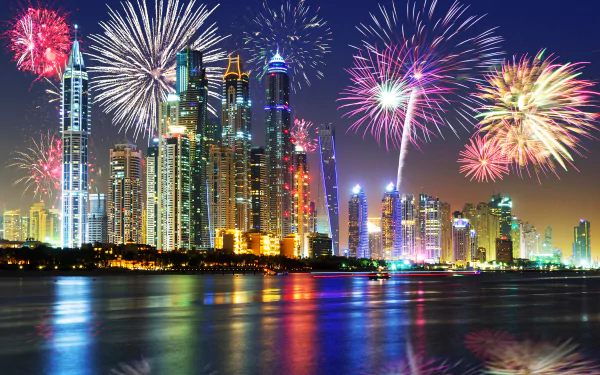 A vibrant nighttime cityscape of Dubai showcases colorful fireworks over stunning skyscrapers, reflecting beautifully in the water, creating a captivating HD wallpaper.