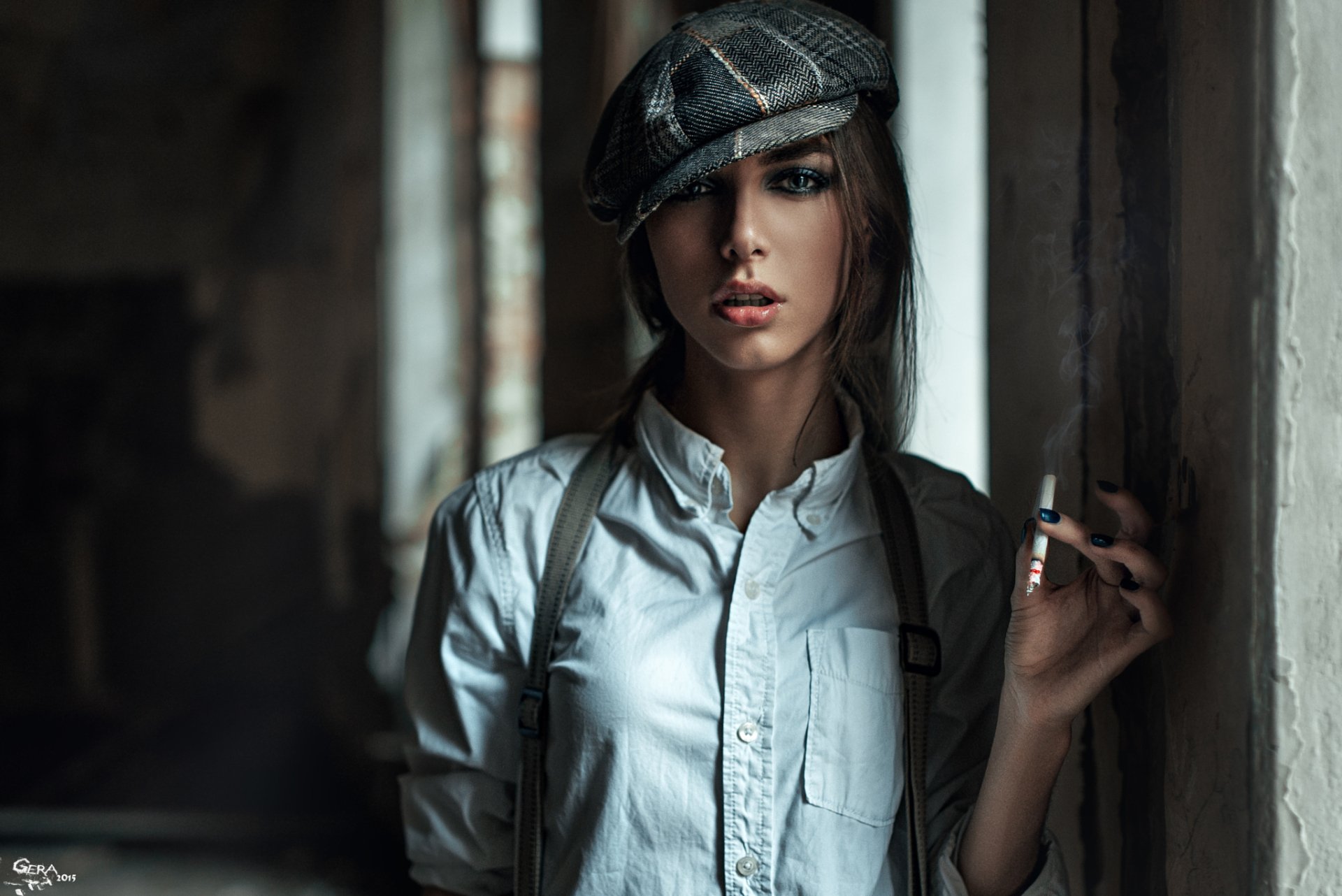 A brunette model wearing a hat stands confidently in a dimly lit space, smoking. The bokeh effect enhances the mood, creating an evocative HD wallpaper background.