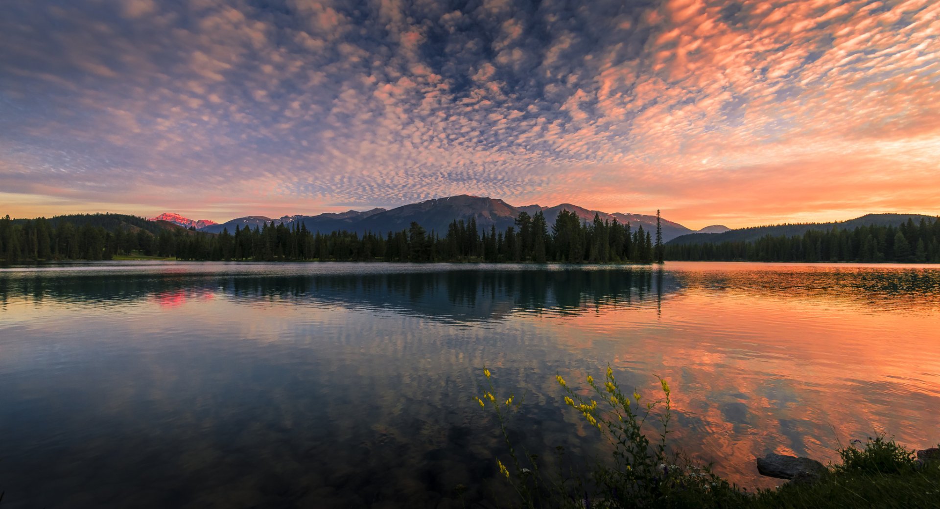 HD PC desktop wallpaper/background: sunset landscape of a forested lake reflecting a dramatic cloud-filled sky, vibrant nature scene with distant mountains.