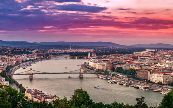 A stunning HD desktop wallpaper of Budapest showcasing the Chain Bridge spanning the river under a vibrant, colorful sky with the cityscape in view.