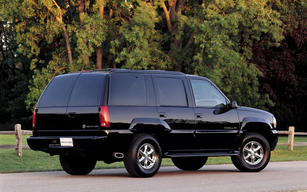 HD desktop wallpaper featuring a black Cadillac Escalade parked on a road with a wooden fence and dense green trees in the background.