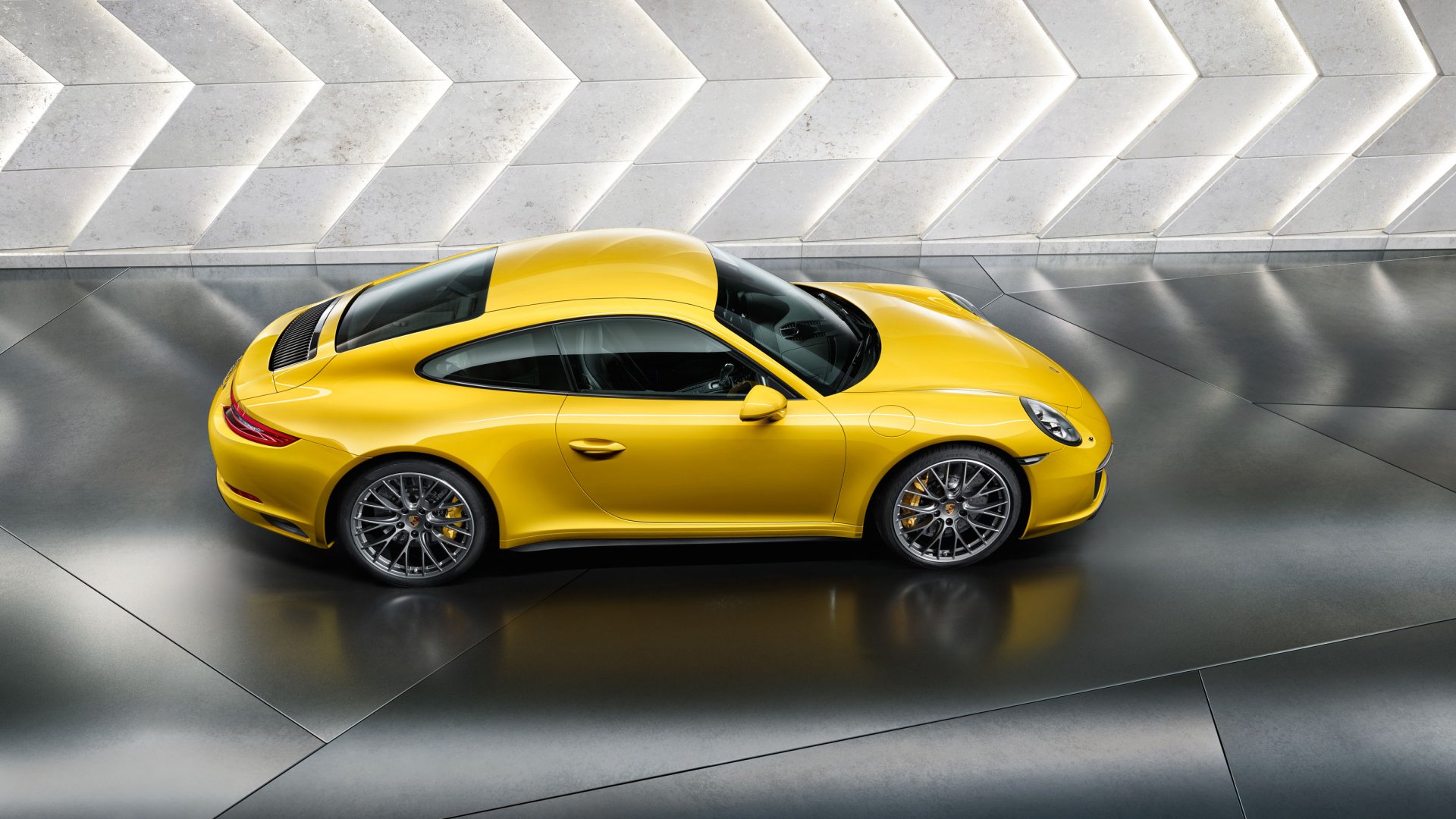 Yellow Porsche 911 Carrera 4S side profile on a reflective floor with geometric white wall backdrop — 2K Quad HD PC desktop wallpaper/background.
