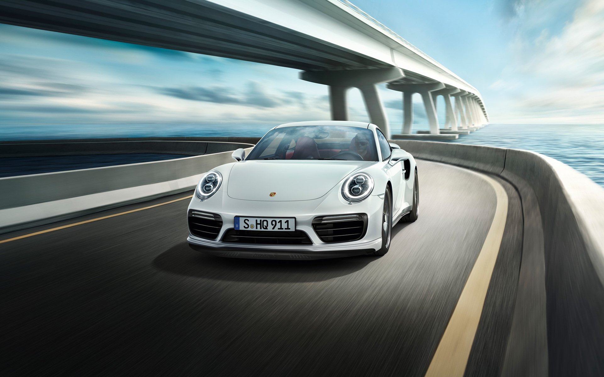 White Porsche 911 Turbo speeding on a coastal highway under a modern bridge, captured in HD for a sleek desktop wallpaper background.