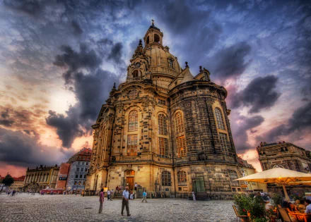 HDR image of Dresden Frauenkirche in Germany under a dramatic cloudy sky, showcasing the detailed architecture of the historic church against a vibrant sunset background.