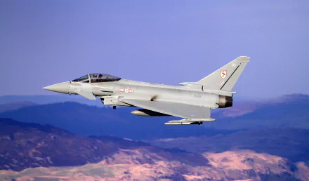 HD desktop wallpaper featuring a Eurofighter Typhoon jet fighter soaring above mountainous terrain with clear blue sky in the background.
