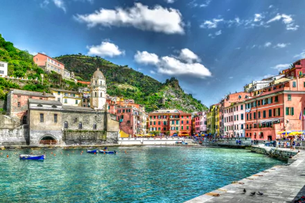 Vibrant 4K HDR view of Manarola, Italy, showcasing colorful buildings, a coastal dome, boats on clear water, and lush mountains under a bright sky.